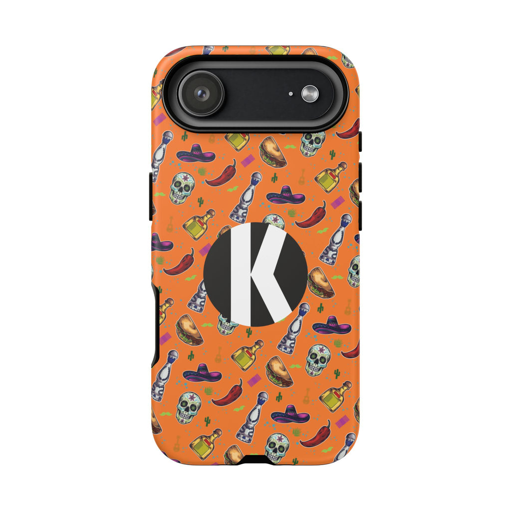 An orange phone case with a festive Mexican-themed pattern of skulls, chili peppers, sombreros, and tequila bottles, featuring a large black circle with a white letter 'K' on the back.