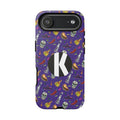 A purple phone case with a Halloween-themed pattern of skulls, chili peppers, bottles, and hats, featuring a large black circle with a white letter 'K' on the back.