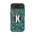 A protective phone case with a teal background and a colorful pattern of skulls, sombreros, and bottles, featuring a large black circle with a white letter 'K' on the back.