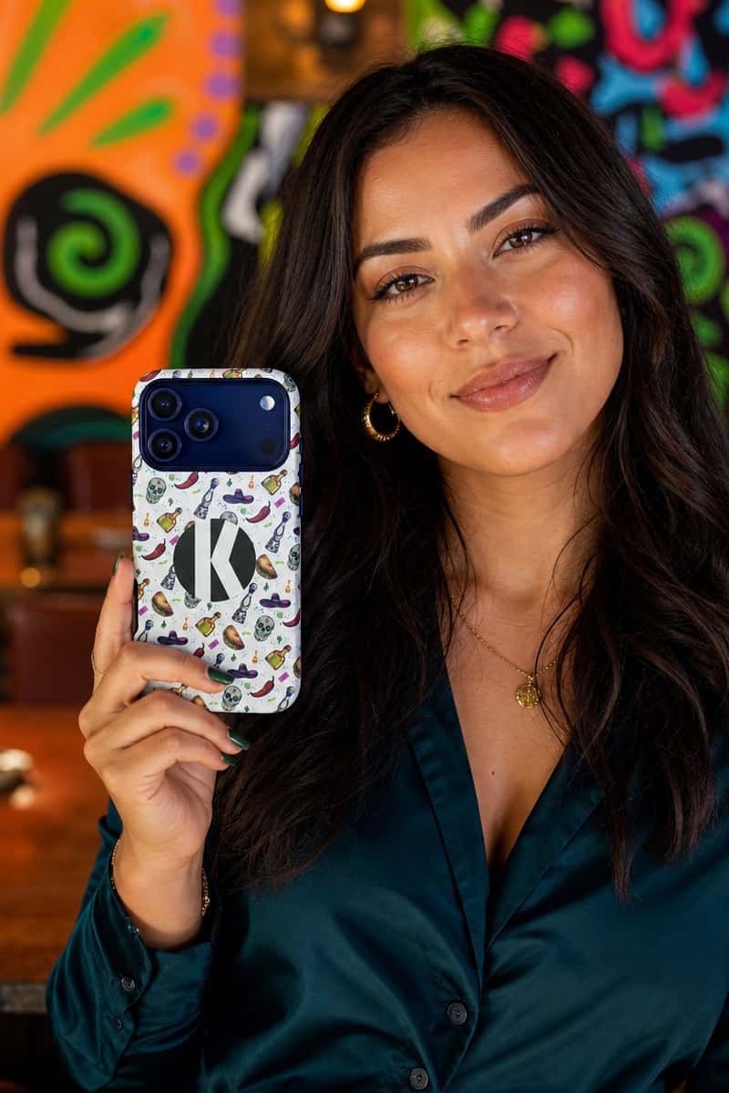 A woman holding a white phone case decorated with colorful cartoon-style illustrations and a large black letter 'K' on the back, set against a vibrant, colorful background.