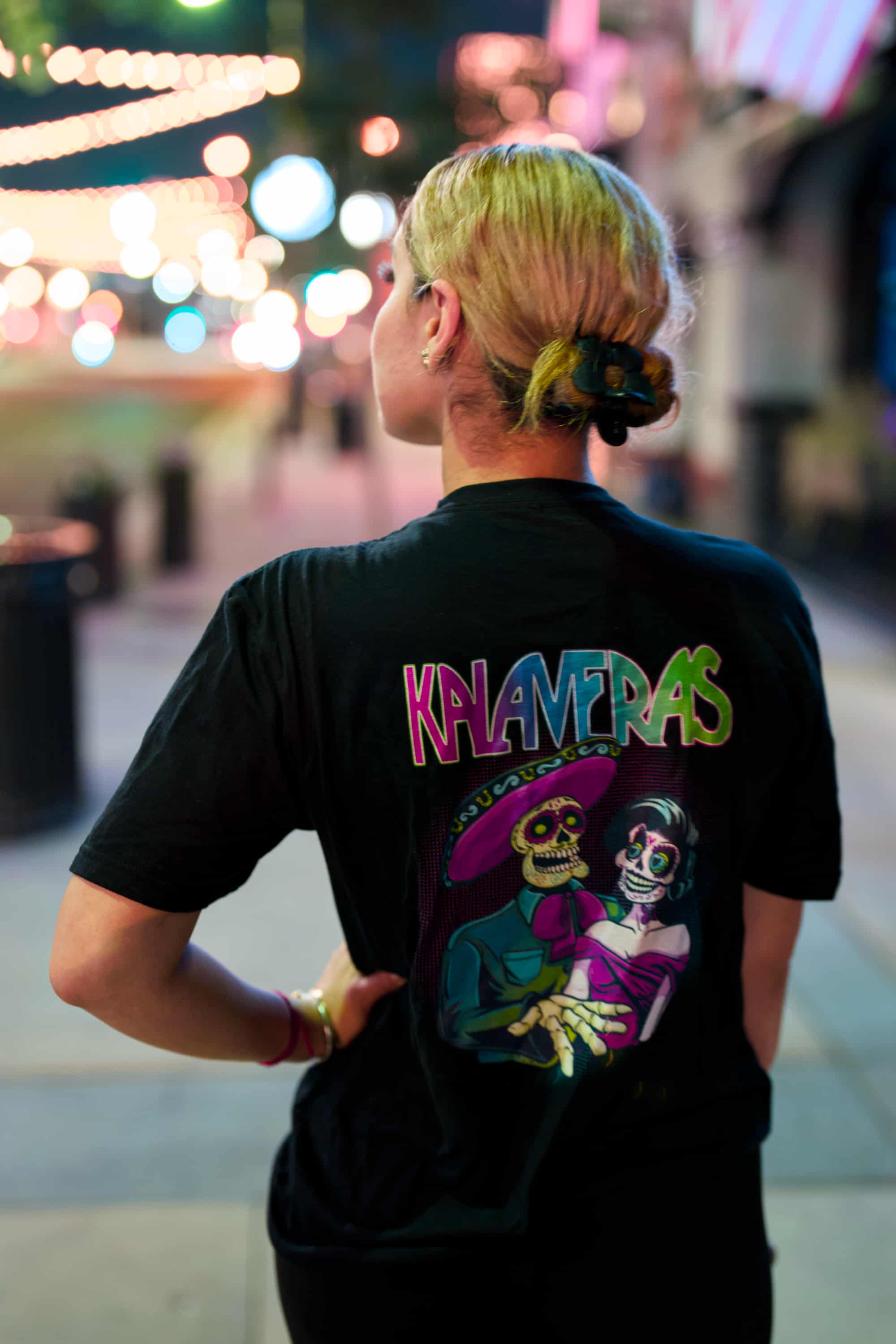 Woman wearing black Kalaveras Heritage Couple Tee back view in a restaurant setting