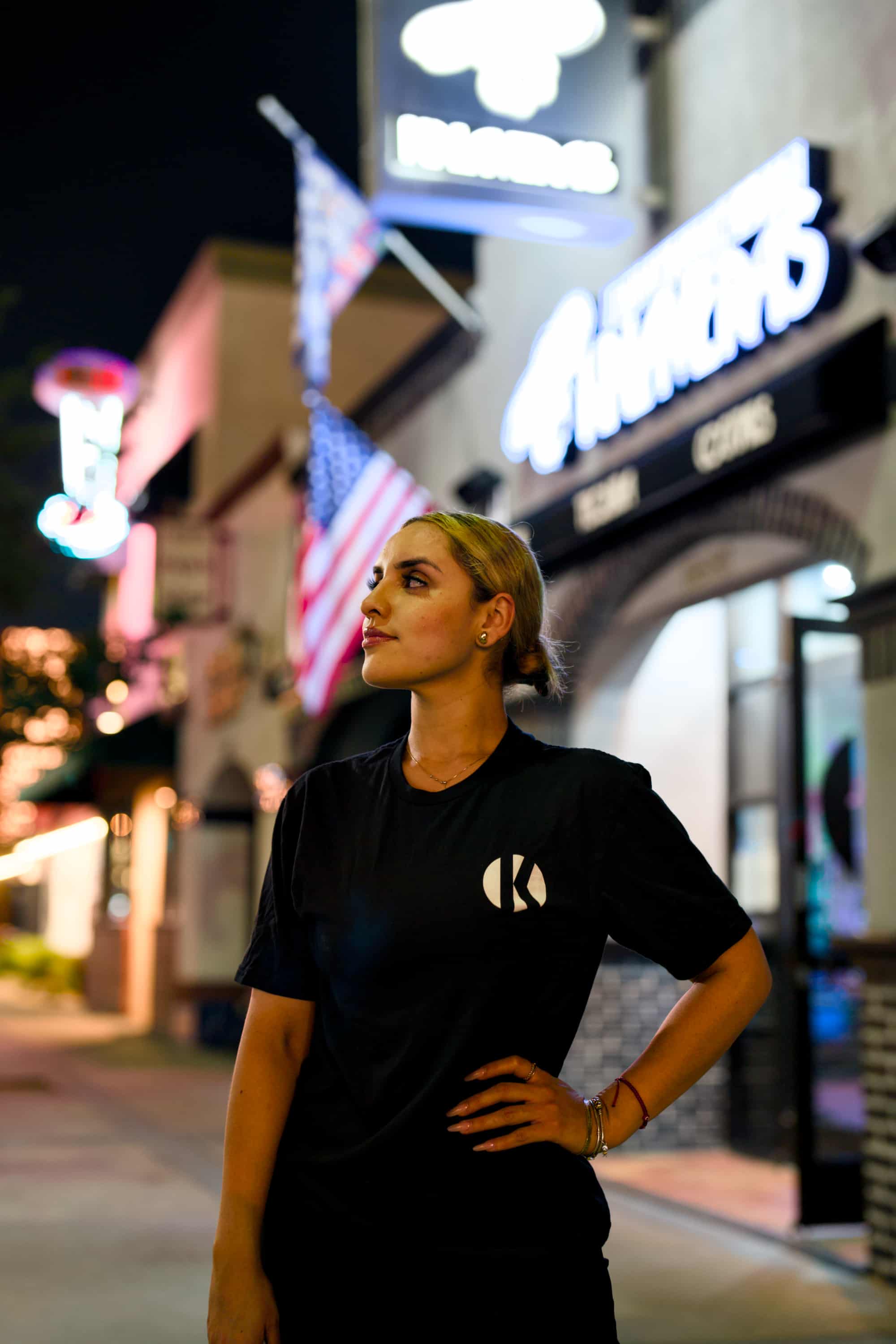 Woman wearing black Kalaveras Heritage Couple Tee front view outside a Kalaveras restaurant at night
