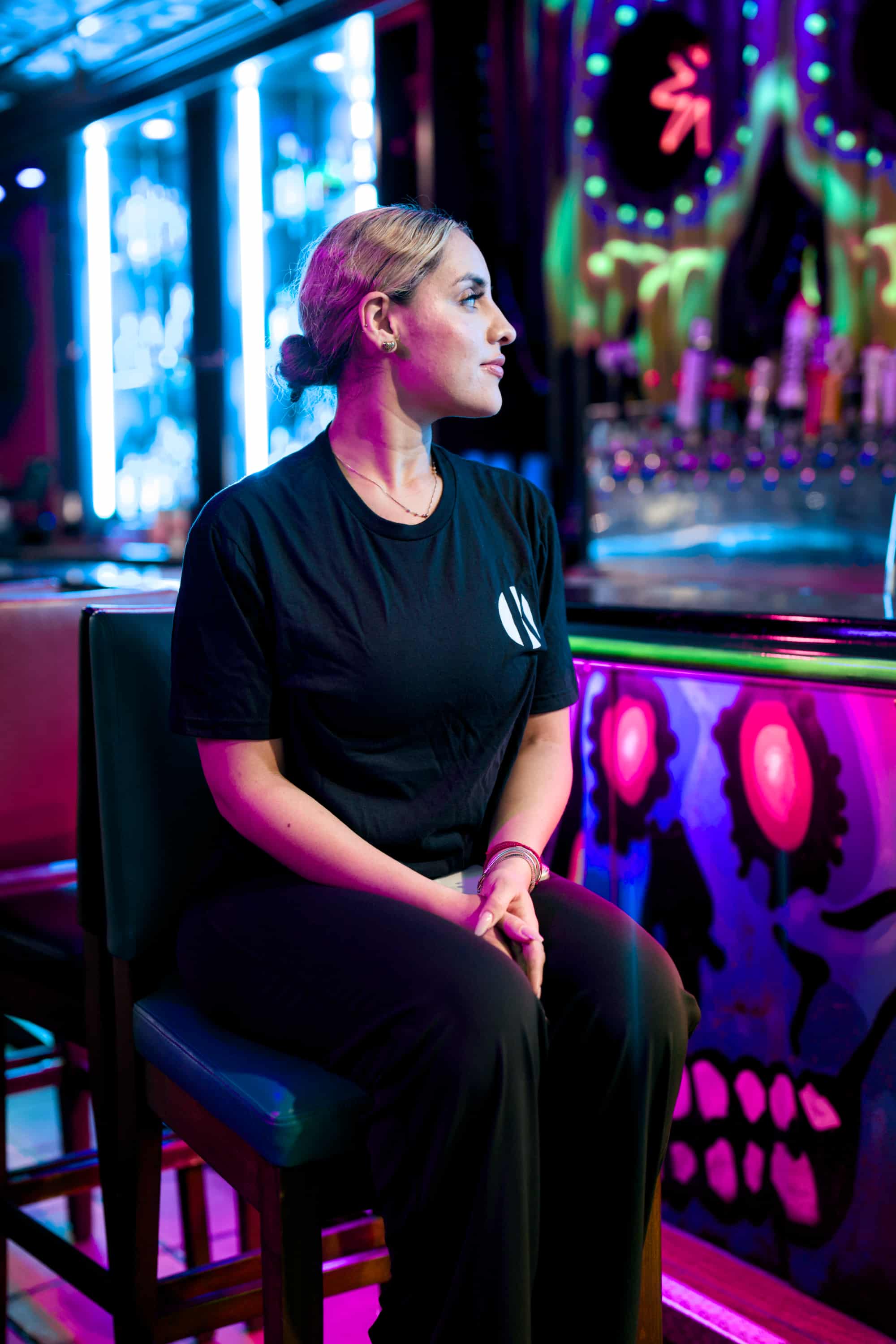 Woman wearing black Kalaveras Taco Tuesday Tee front view seated inside a restaurant
